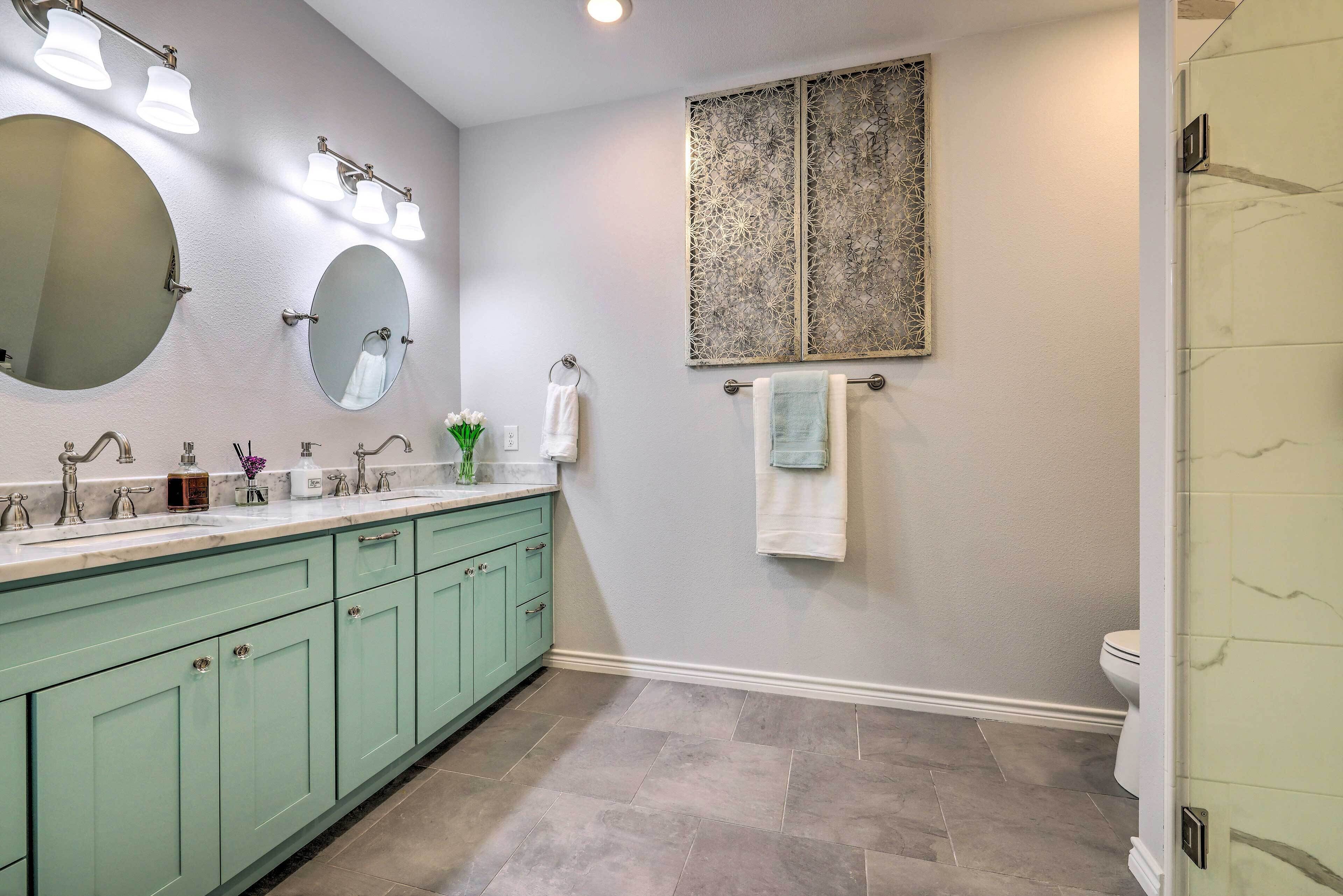 A bathroom with a vanity, two mirrors, a sink, a toilet, and a shower area.