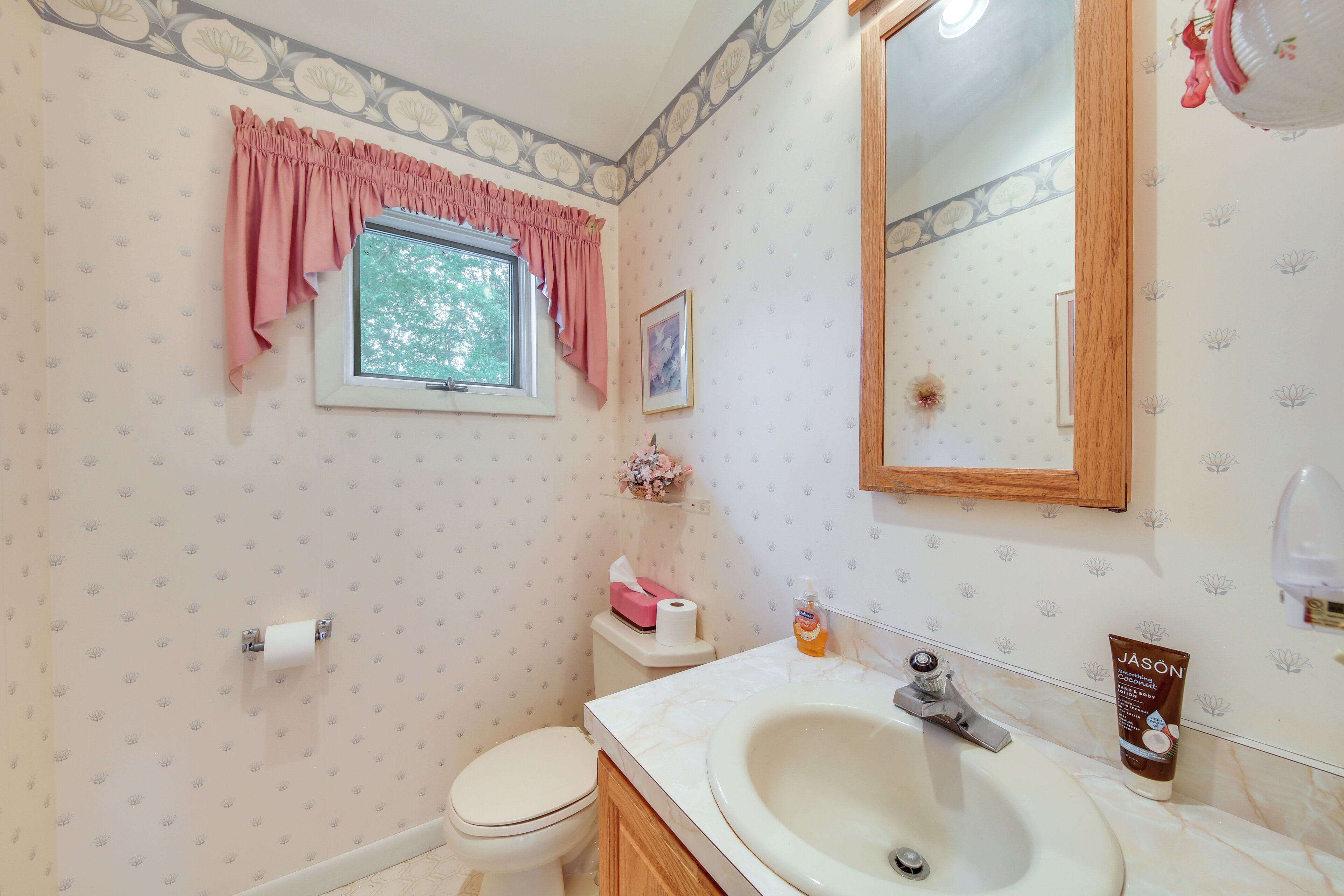 A bathroom with a toilet, sink, mirror, and window with curtains.