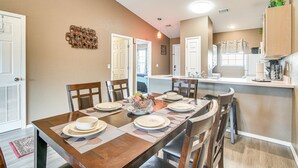 A dining area with a wooden table set for six, surrounded by chairs, with a kitchen in the background. - Stunning Table Rock Lake Condo Near Branson Strip! (Branson)