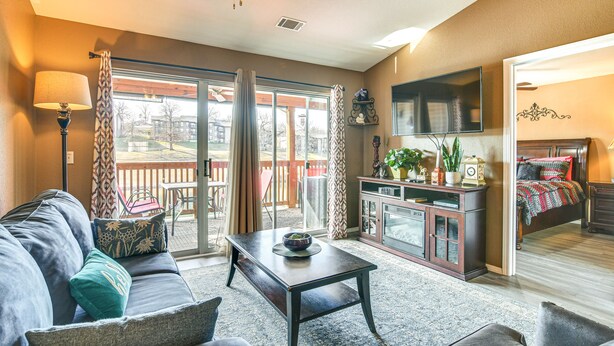 A living room with a sofa, coffee table, and a TV mounted on the wall. There is a sliding glass door leading to a balcony. - Stunning Table Rock Lake Condo Near Branson Strip! (Branson)