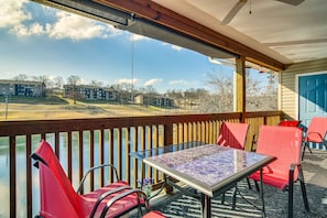 A covered outdoor area with a table and chairs, overlooking a body of water and buildings in the distance. - Stunning Table Rock Lake Condo Near Branson Strip! (Branson)