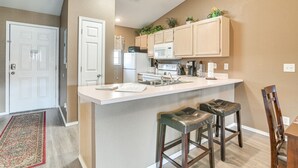 A kitchen with a white island, wooden cabinets, and a microwave. There are two bar stools and a wooden chair. - Stunning Table Rock Lake Condo Near Branson Strip! (Branson)