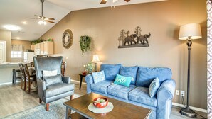 A living room with a blue sofa, a leather armchair, a coffee table, and a dining area with wooden chairs and a table. - Stunning Table Rock Lake Condo Near Branson Strip! (Branson)