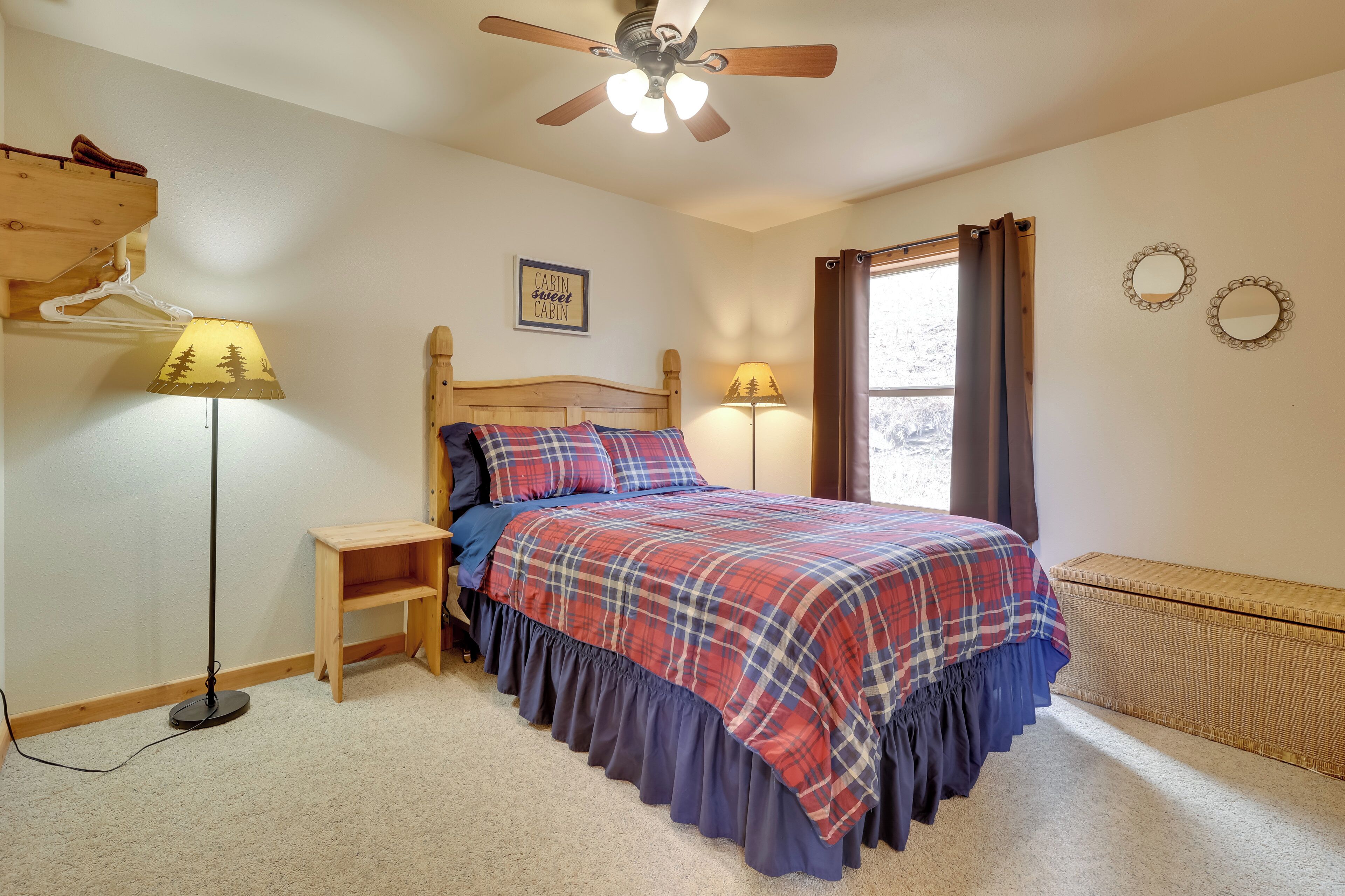 A bedroom with a bed, two bedside lamps, a ceiling fan, a window with curtains, and a small wooden shelf.