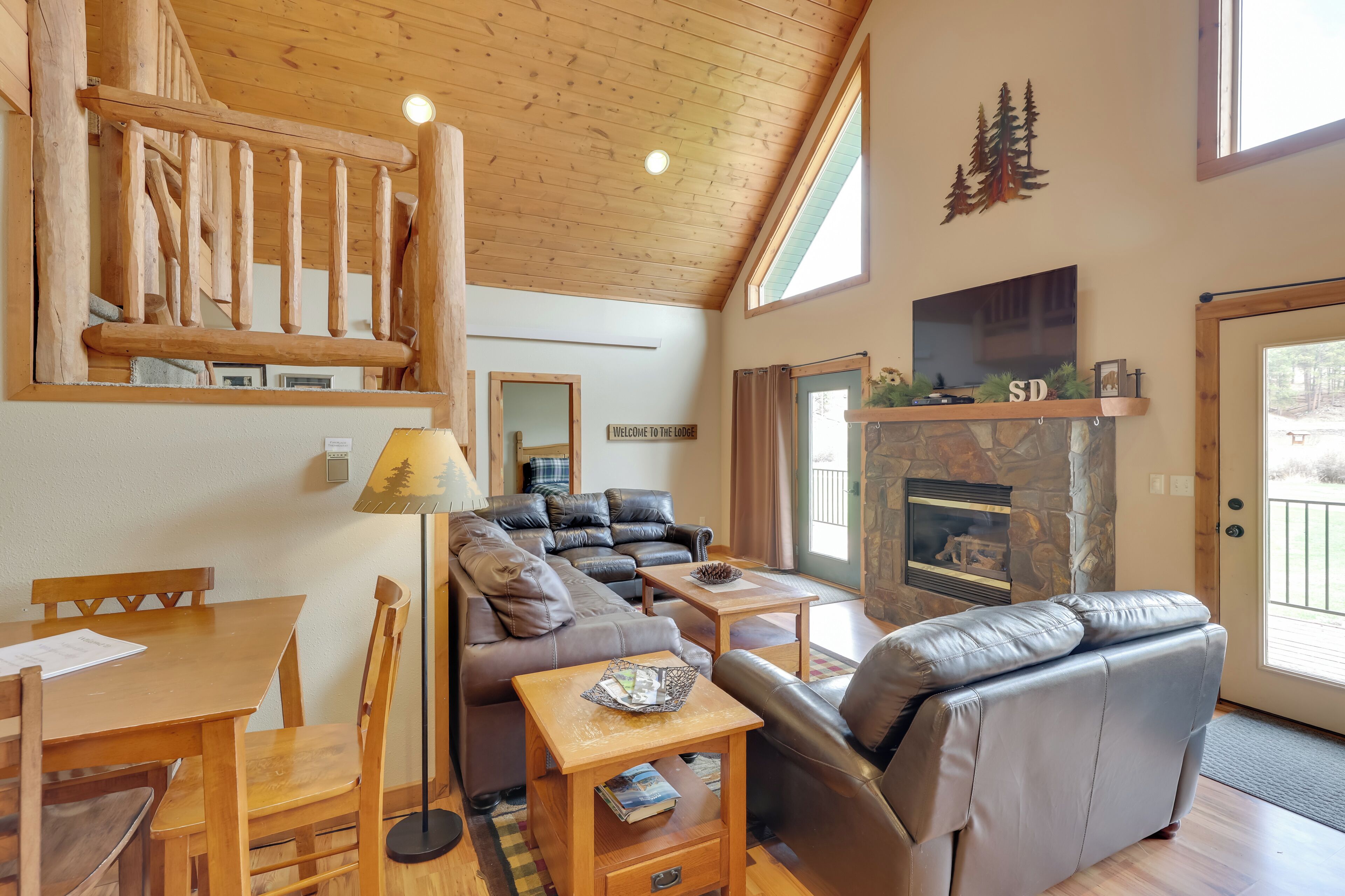 A cozy lodge interior with a wooden staircase, a fireplace, a sofa, and a dining area.