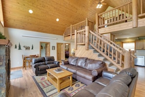 A spacious living area with a wooden staircase, leather sofas, and a dining table. - Cabin w/ On-site Trails - 15 Miles to Mt Rushmore! (Hill City)