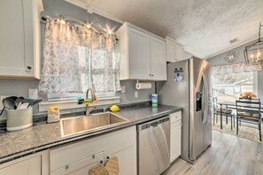 A modern kitchen with white cabinets, a stainless steel refrigerator, a dishwasher, and a window with floral curtains. - 1/2 Mi to Fort Campbell: 'state Line Retreat' (Clarksville)