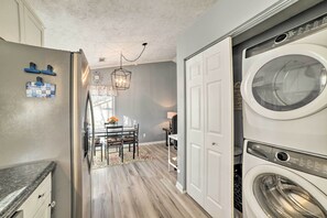A laundry room with a front-loading washer and dryer, a dining area with a table and chairs, and a kitchen area with a refrigerator and cabinets.