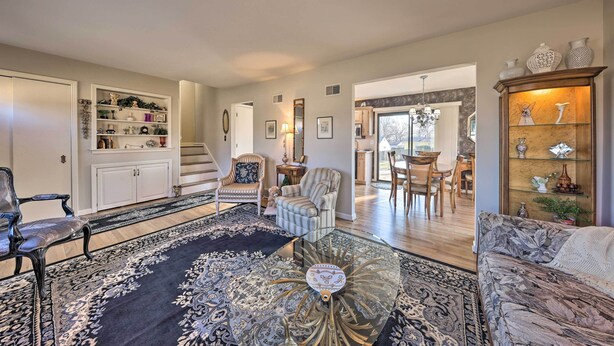 A spacious living room with a large rug, a glass coffee table, and a sofa. There is a bookshelf, a dining area, and a staircase leading to another level. - Cozy Kansas City Home w/ Yard - 9 Mi to Dtwn! (Kansas City)