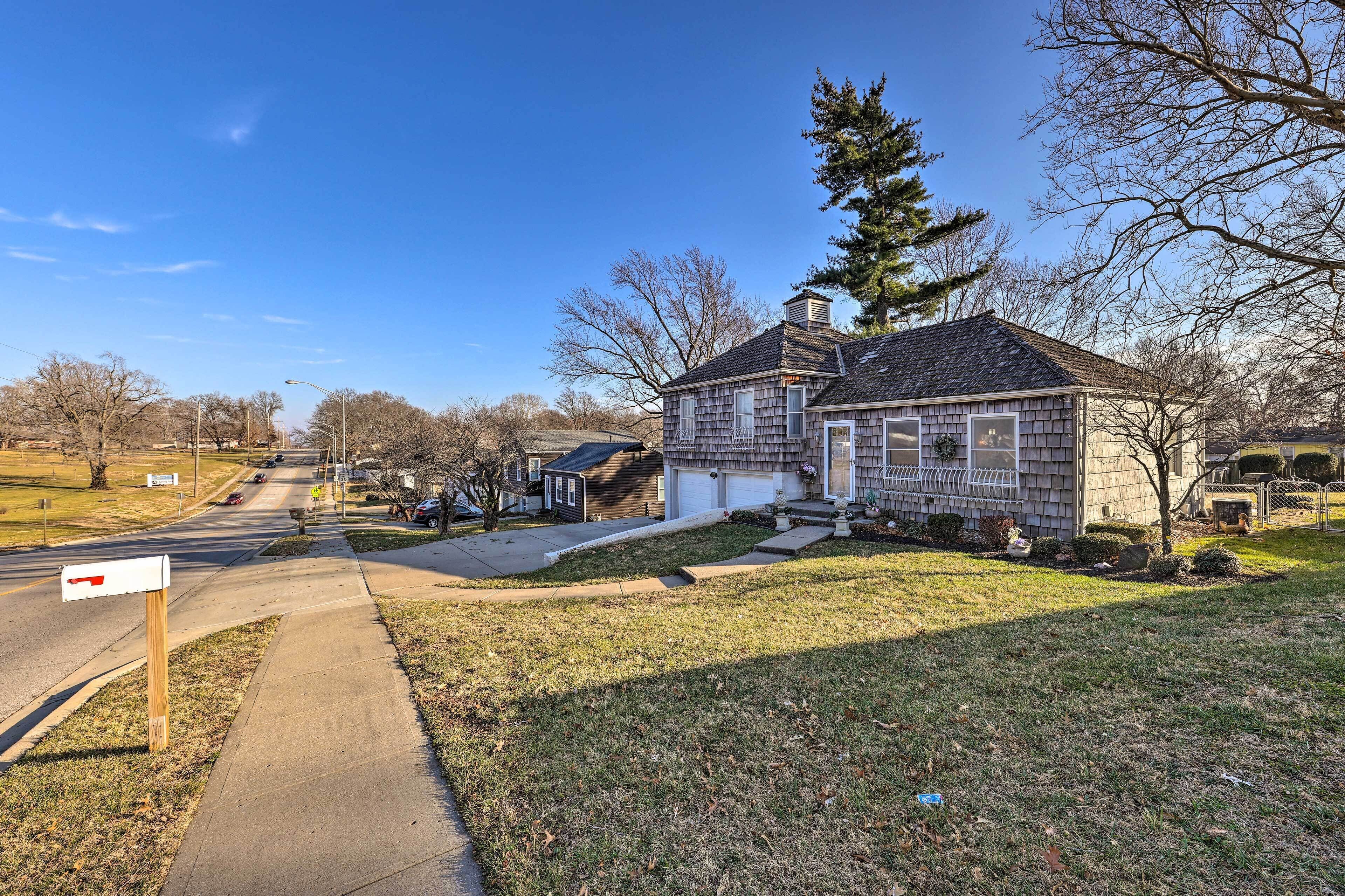 A residential house with a garage, a front yard with a small tree, and a mailbox on the sidewalk.