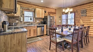 A rustic cabin-style kitchen with wooden cabinetry, a stone accent wall, a stainless steel refrigerator, and a dining area with wooden chairs and a table. - Dock w/ Boat Slip: Cozy Cabin Near Leesville Lake! (Pittsville)