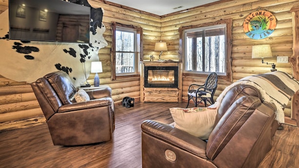 A log cabin interior with leather sofas, a fireplace, a mounted TV, and a 'Welcome to the Lake' sign. - Dock w/ Boat Slip: Cozy Cabin Near Leesville Lake! (Pittsville)