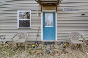 Una casa con una puerta azul, dos sillas de plástico y un camino de piedra que lleva a la puerta.