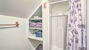 A bathroom with a shower curtain featuring a shell pattern, a towel rack, and shelves with folded towels. - Cozy Bingham Apt, 1 Mi to Rafting & ATV Trail (Bingham)