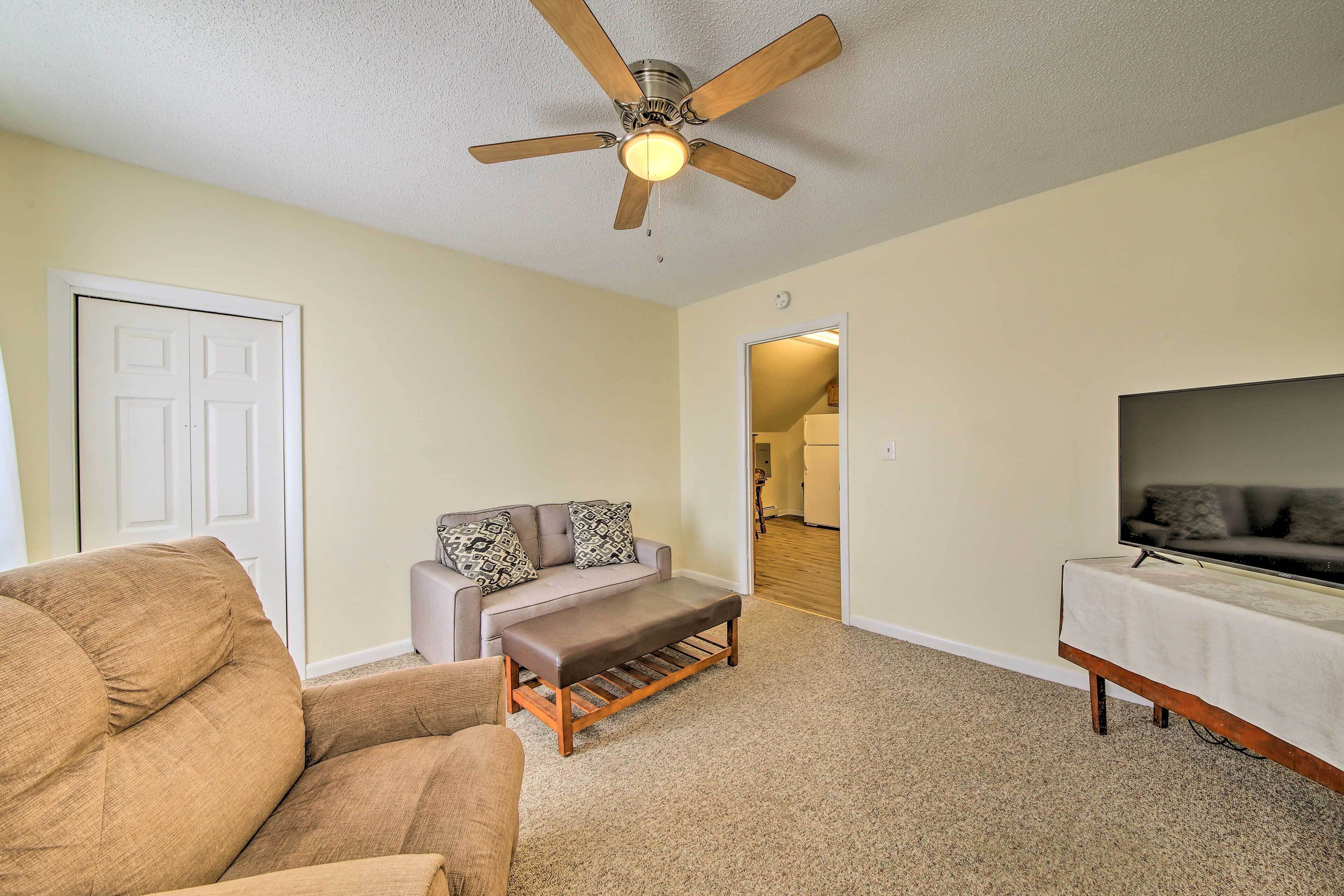 A living room with a ceiling fan, a sofa, a bench, and a TV stand.