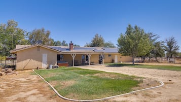 A single-story house with a covered patio, a lawn, and a hose.