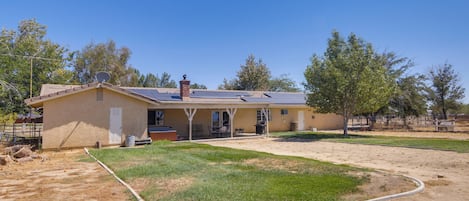 A single-story house with a covered patio, a lawn, and a hose.