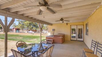 A covered patio with a table and chairs, a ceiling fan, and a hot tub.