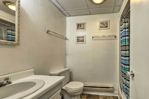 A bathroom with a white sink, toilet, and shower. There are three framed pictures on the wall. - 1 Ocean Fun:' Emerald Isle Apt, Steps to Beaches! (Emerald Isle)