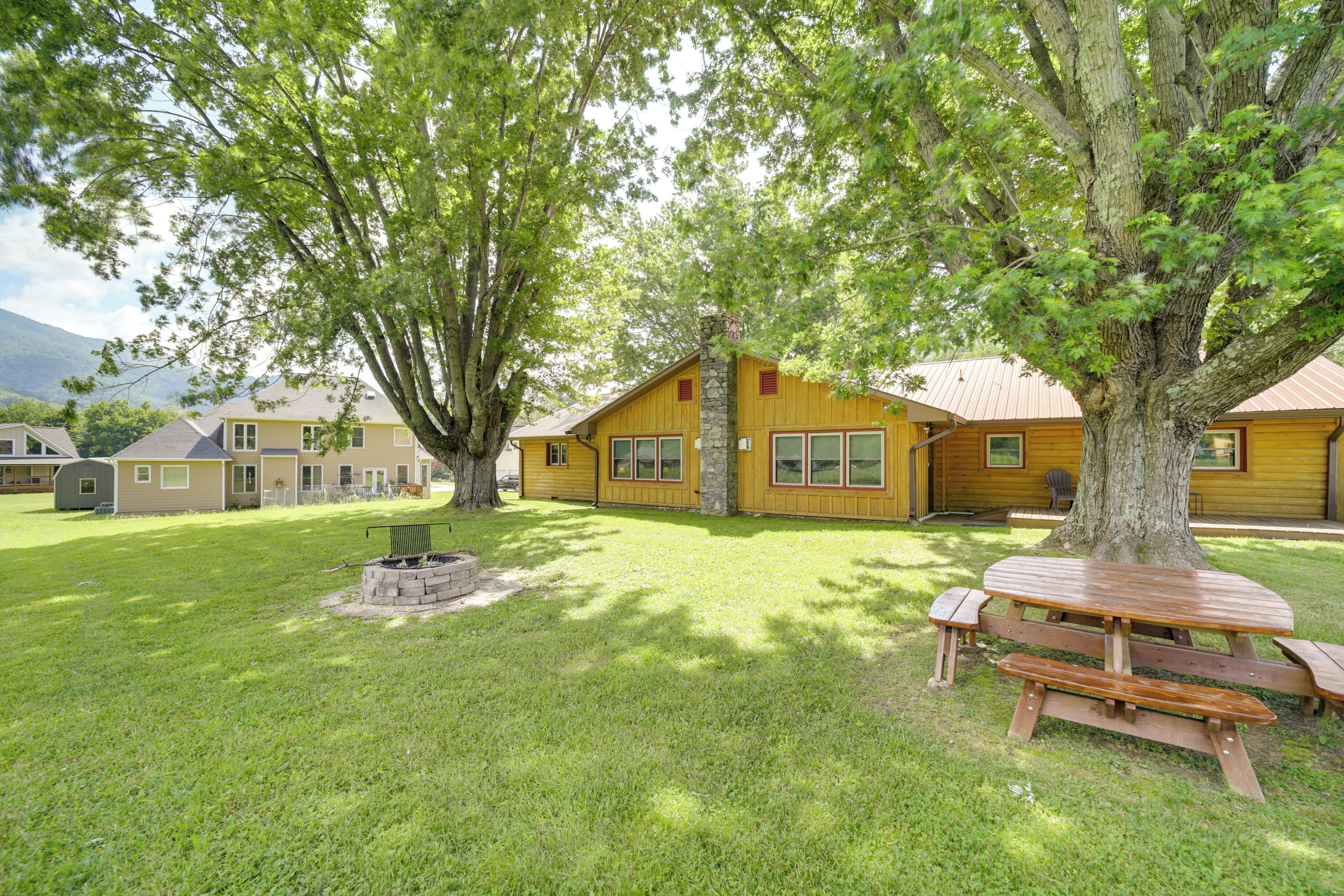 Une cabane en bois avec une cheminée en pierre, entourée d’une pelouse bien entretenue et de grands arbres.