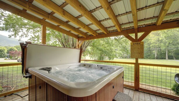 Een bubbelbad onder een houten pergola met uitzicht op een gazon en bomen.