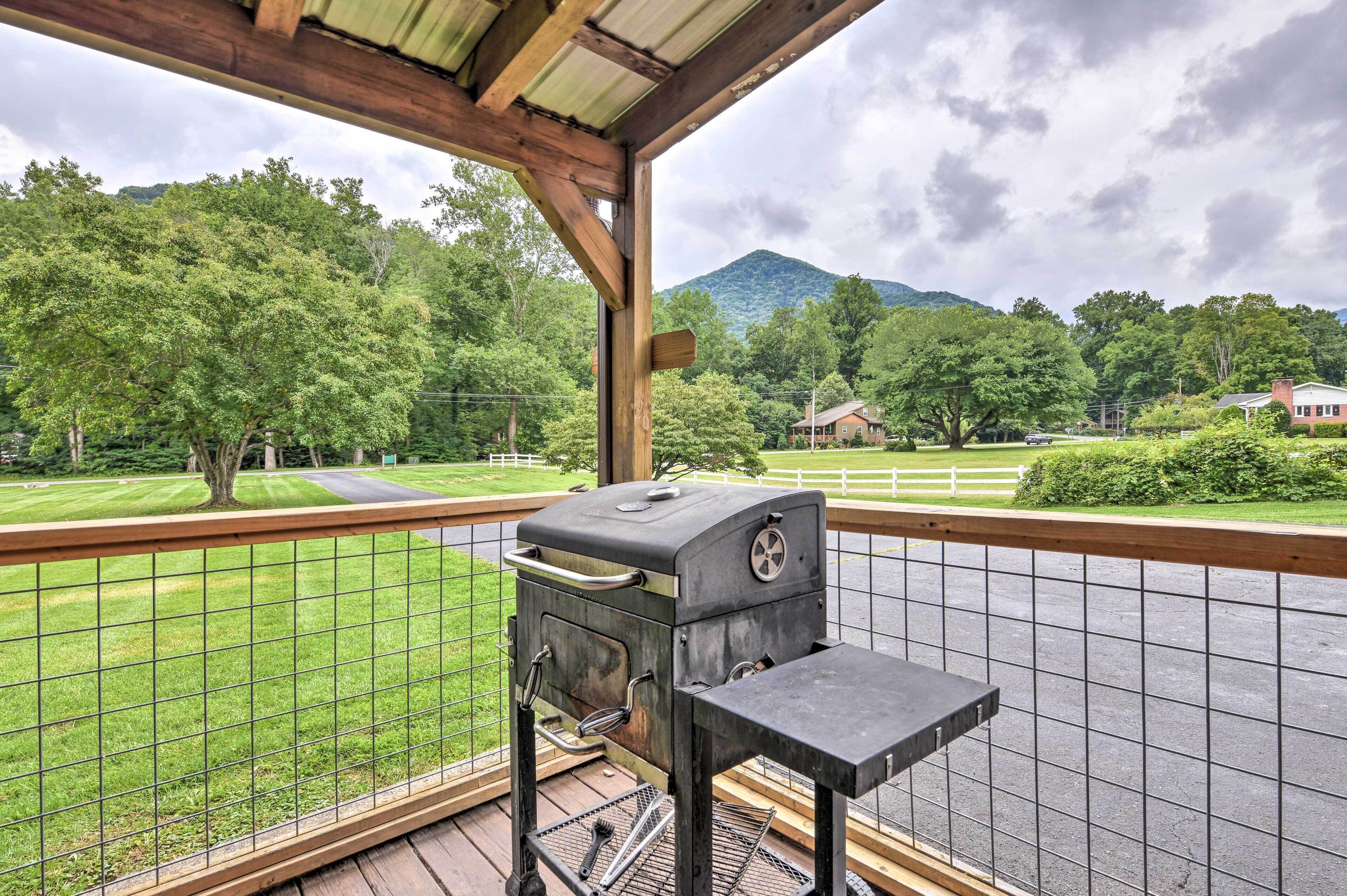 Ein überdachter Außenbereich mit Grill und Tisch, der auf eine grüne Landschaft und einen Berg blickt.