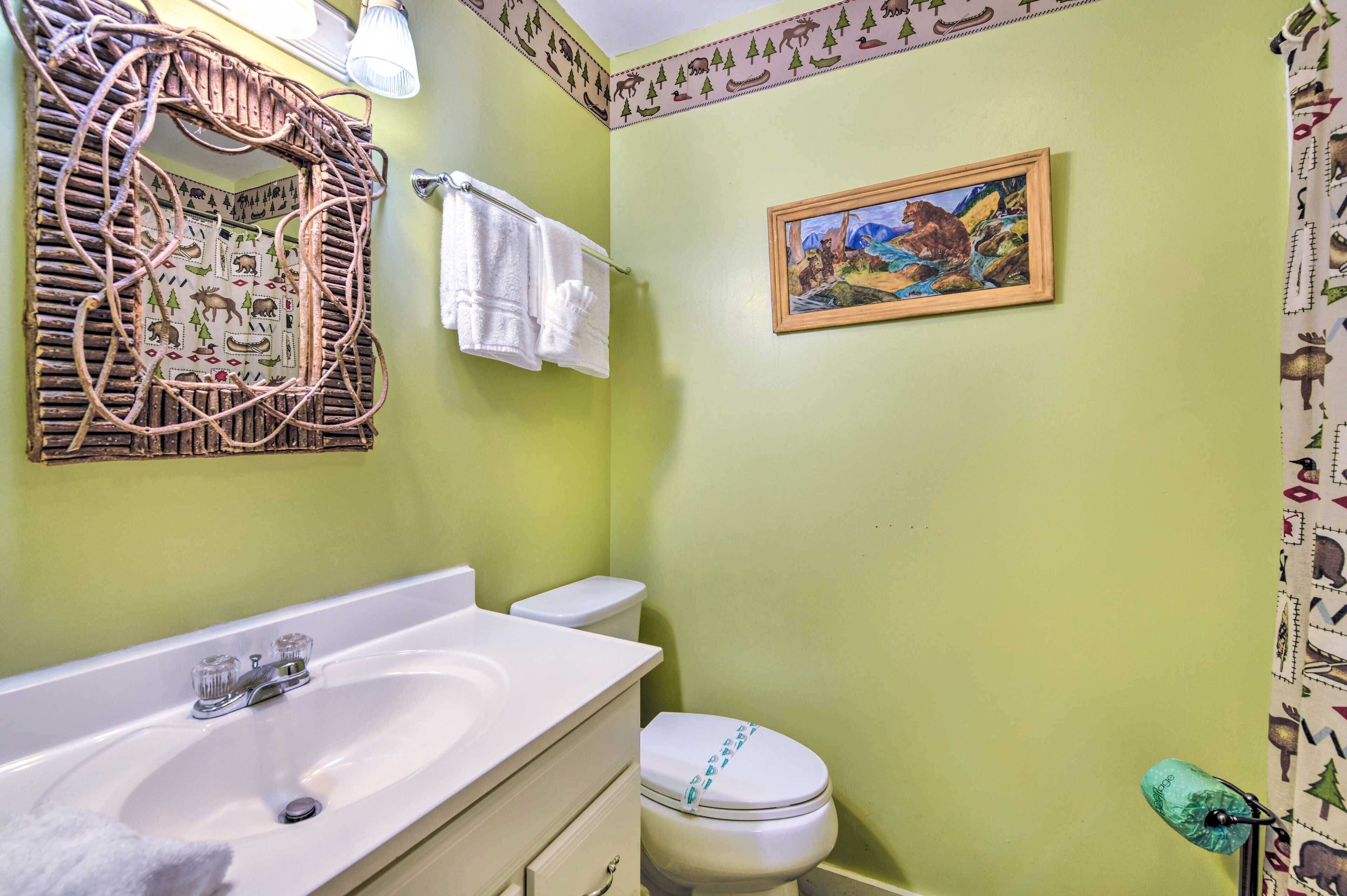 A bathroom with a white sink, a toilet, and a mirror with a woven frame. There is a towel rack with white towels and a framed picture on the wall.