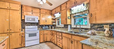 A kitchen with wooden cabinets, a microwave, stove, granite countertop, and a ceiling fan.