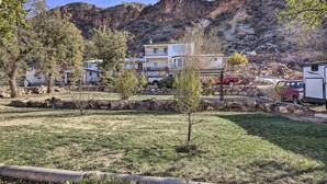 A two-story building with a balcony, surrounded by a grassy area and trees, with a rocky mountain in the background. - On-site Trails! Hot Tub Hideaway in Zion Area (Hurricane)
