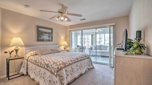 A bedroom with a large bed, a ceiling fan, a nightstand with a lamp, a dresser, and a sliding glass door leading to a balcony. - Branson Condo w/ Sunroom Near Downtown! (Branson)
