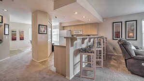 A modern kitchen with a built-in microwave, a bar area with a cushioned stool, and a gray recliner. - Branson Condo w/ Sunroom Near Downtown! (Branson)