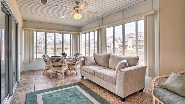 A sunroom with a large window, a ceiling fan, a sofa, a dining table with chairs, and a rug. - Branson Condo w/ Sunroom Near Downtown! (Branson)
