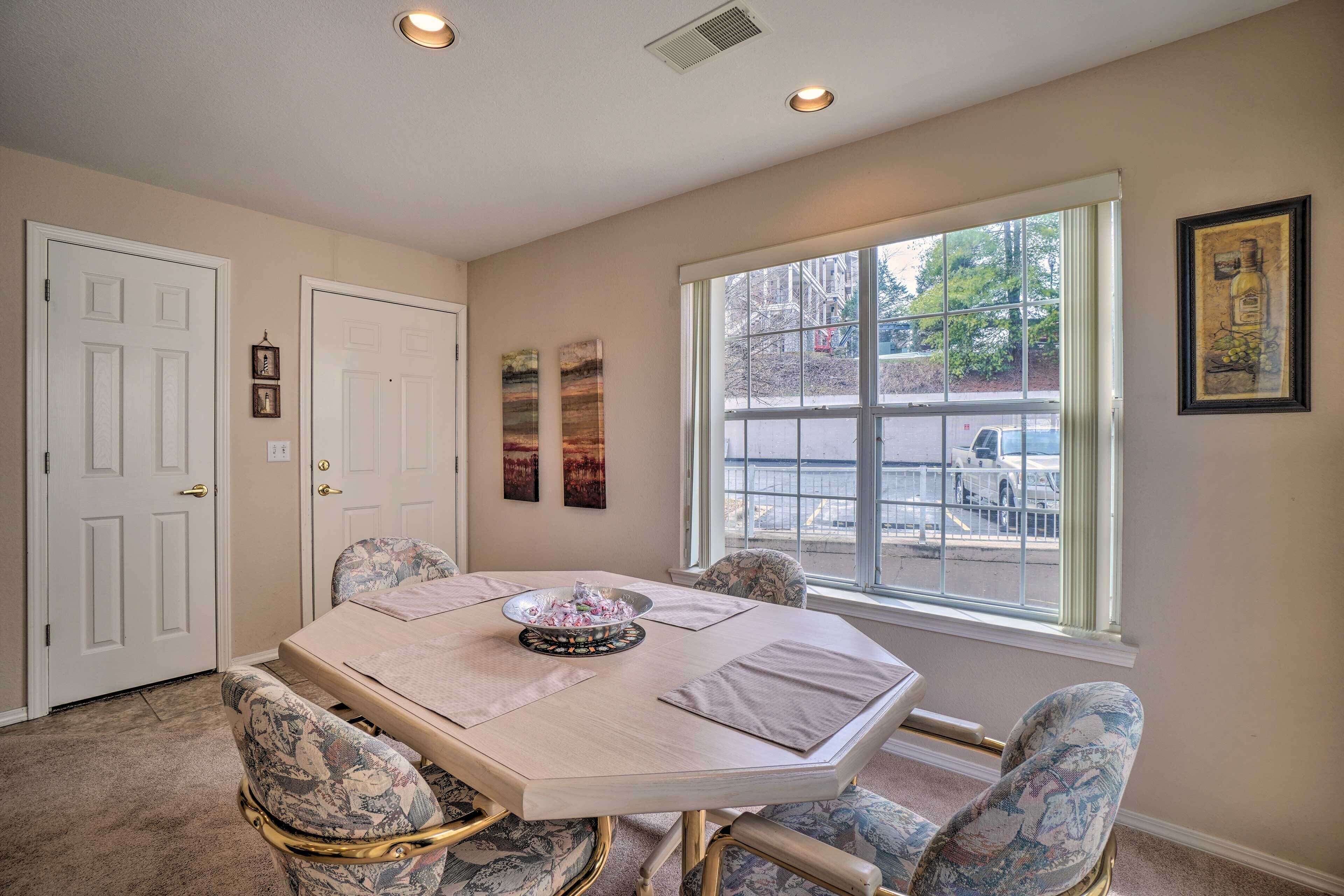 A dining room with a large oval table, four chairs, and a window with a view of the street.
