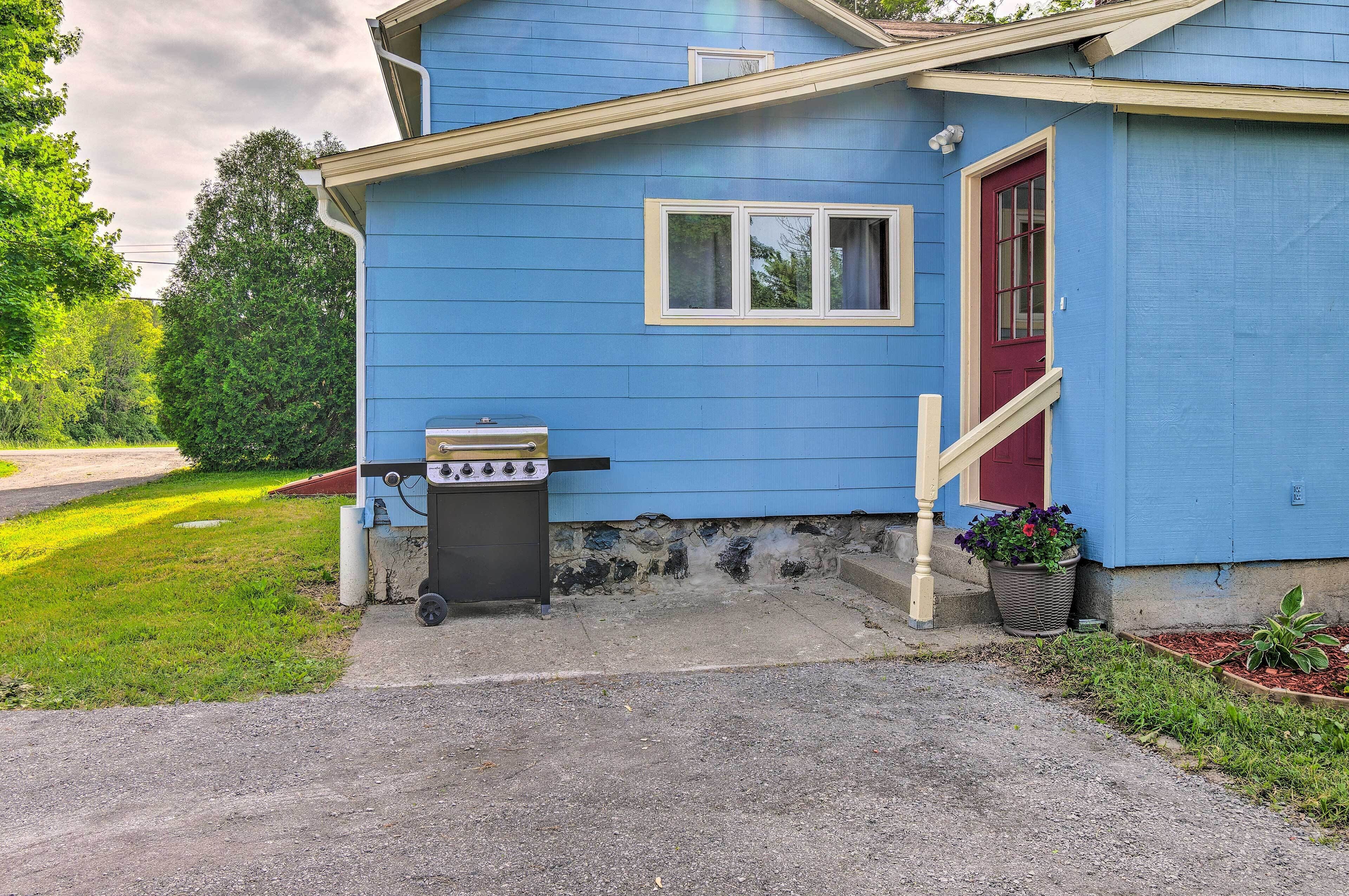 A blue house with a red door, a small porch, and a barbecue grill.