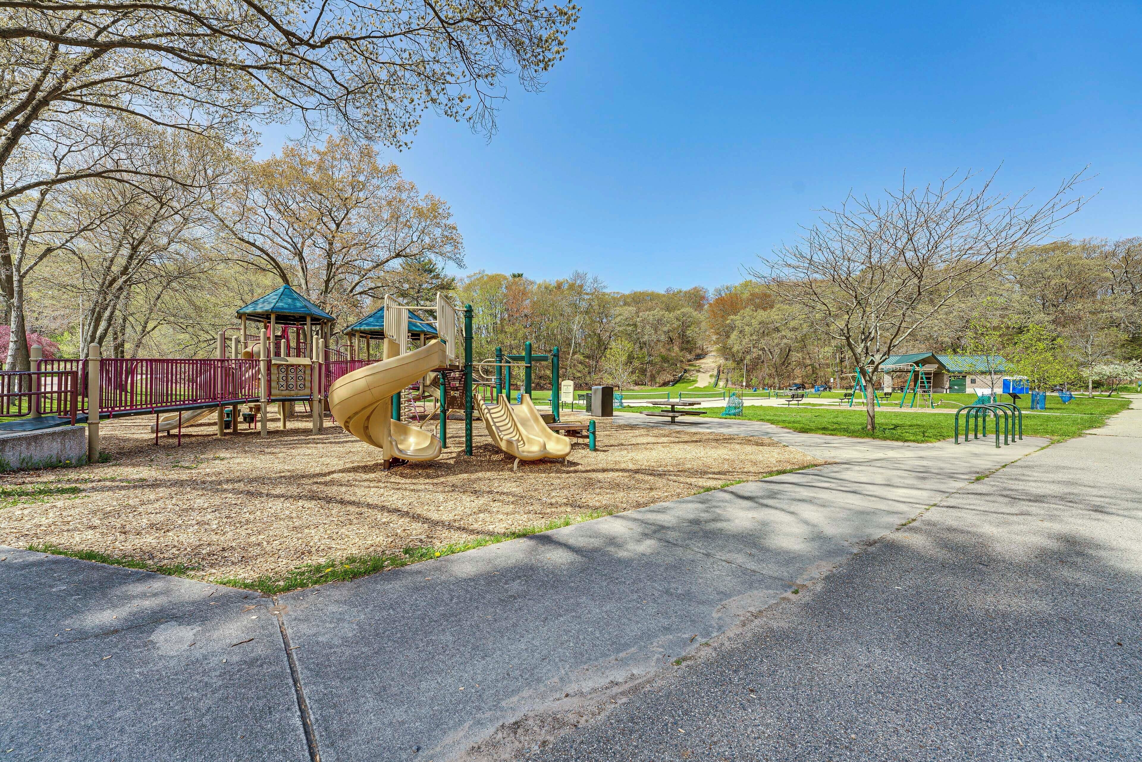 Ein Spielplatz mit Rutschen und Klettergerüsten, umgeben von Bäumen und einem klaren Himmel.