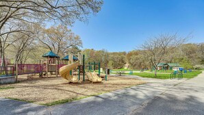 A playground with slides and climbing structures, surrounded by trees and a clear sky. - Walk to Beach: Lake Michigan Getaway! (Muskegon)