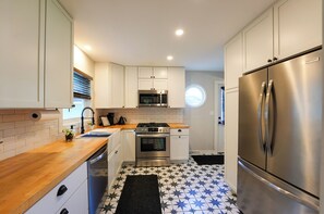 A compact kitchen with white cabinets, a stainless steel refrigerator, a microwave, and a stove. - Walk to Beach: Lake Michigan Getaway! (Muskegon)