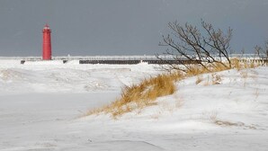 A red lighthouse on a snowy beach with a pier extending into the water. - Walk to Beach: Lake Michigan Getaway! (Muskegon)