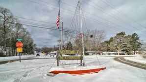 A snowy road with a stop sign, an American flag, and a welcome sign for Beachwood. - Walk to Beach: Lake Michigan Getaway! (Muskegon)