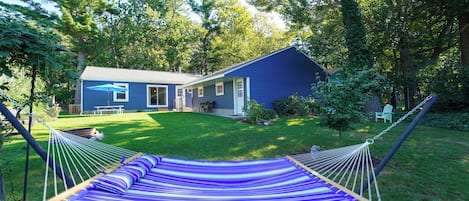 A hammock in a grassy yard with a house in the background.