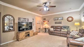 A living room with a large flat-screen TV, a ceiling fan, a brown leather sofa, a wooden entertainment unit, and a 'Family' sign on the wall.
