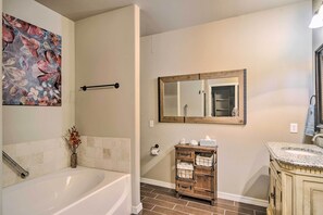 A bathroom with a bathtub, a wooden vanity with drawers, a mirror, and a floral artwork on the wall. - Inviting Amarillo Gem Near Palo Duro Canyon! (Amarillo)