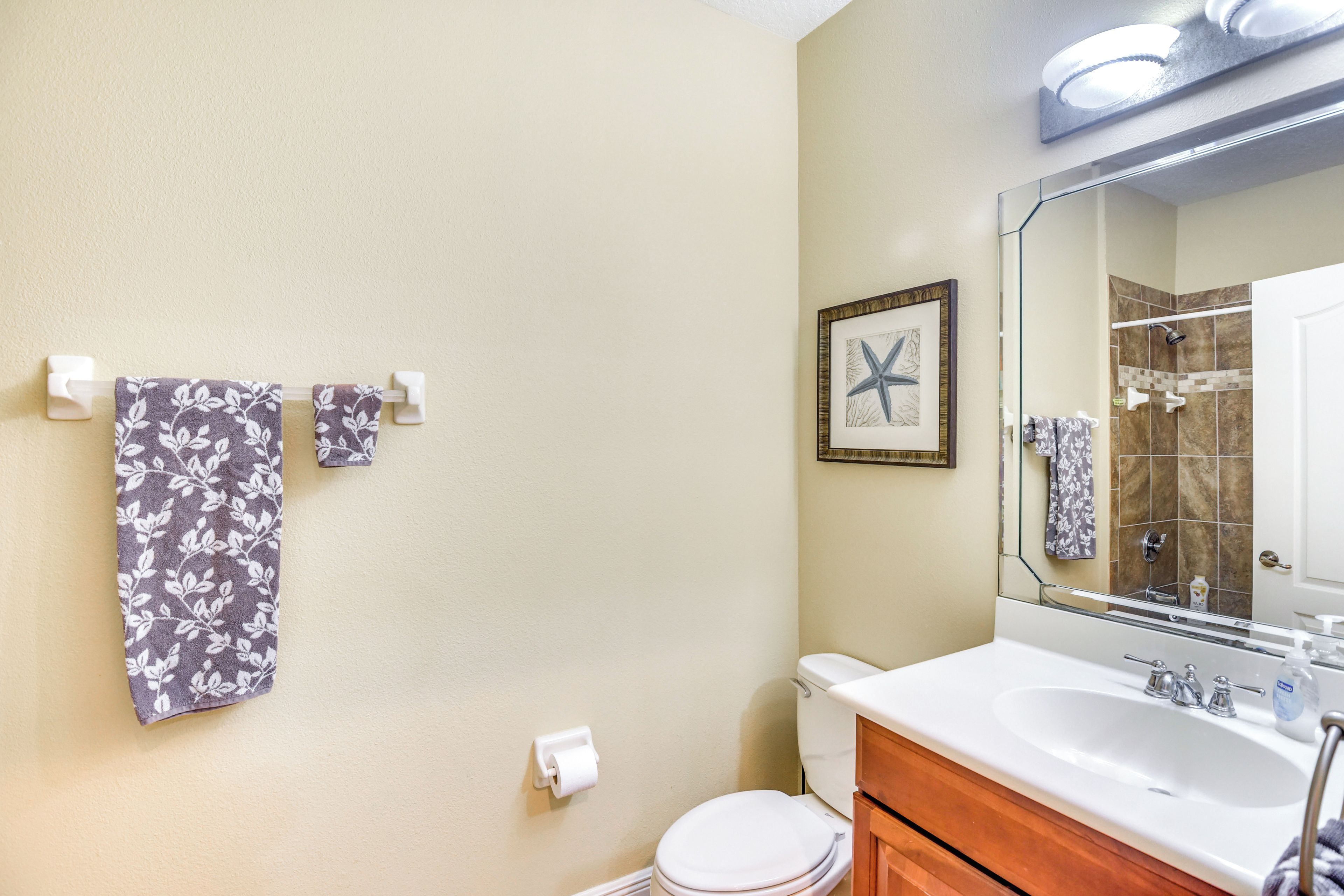 A bathroom with a toilet, sink, and mirror. There are towels hanging on a rack and a framed picture on the wall.