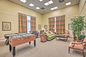 A room with a foosball table, a sofa, a chair, a lamp, and a potted plant.