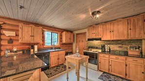 A wooden cabin kitchen with granite countertops, wooden cabinets, a central island, and a stone backsplash. - Riverfront Troy Cabin Ready With Bikes & Rafts! (Troy)