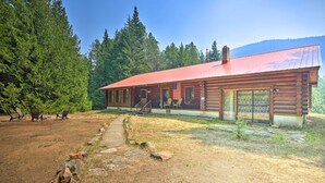 A log cabin with a red roof, a porch with chairs, and a stone pathway leading to the entrance. - Riverfront Troy Cabin Ready With Bikes & Rafts! (Troy)