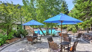 An outdoor patio area with stone flooring, metal chairs, and blue umbrellas. - Big Sky Condo w/ Mountain Views, Hike, Ski & Fish! (Big Sky)