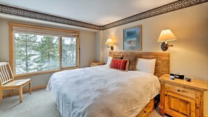 A bedroom with a large window, a wooden headboard, a bedside table with a lamp, and a nightstand. - Big Sky Condo w/ Mountain Views, Hike, Ski & Fish! (Big Sky)