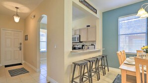 A kitchen with a microwave, oven, and a bar area with stools. There is a door leading to another room and a window with blinds. - 10 Mi to Disney: Resort Getaway w/ Balcony! (Davenport)