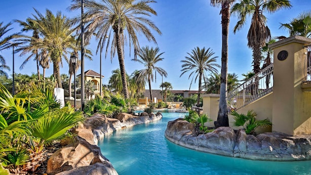 A pool area with clear blue water, surrounded by rocks and palm trees. - 10 Mi to Disney: Resort Getaway w/ Balcony! (Davenport)